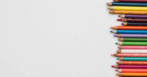 A picture of an assortment of colored pencils lined up sideways on the right hand side of a grey background.