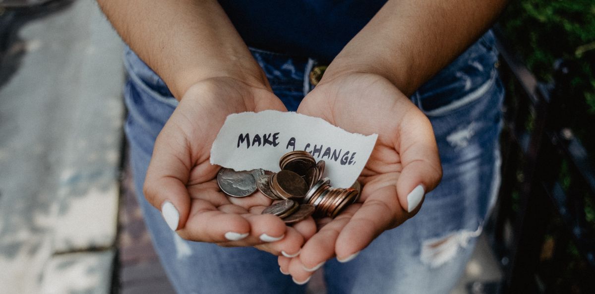 A person holding with both hands together cents, quarters, nickels and dimes along with a piece of paper that says Make A Change