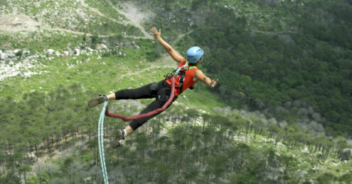 nonprofit executive director - a woman with tanned skin is jumping out over a landscape with trees attached to a bungee cord