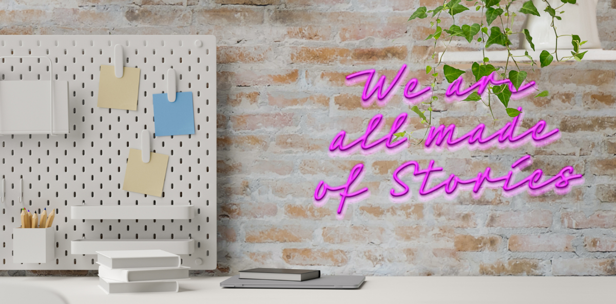Desk with notebooks, pens and other office tools and a purple neon sign that reads "We are all made of stories"