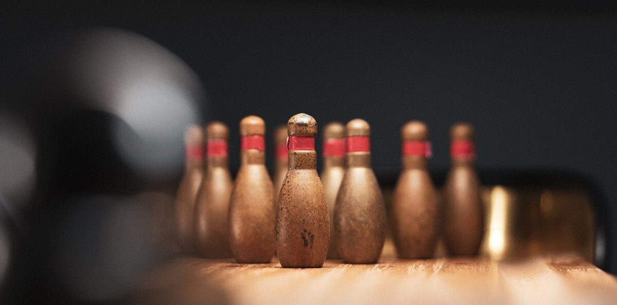 nonprofit blogs - Ten vintage bowling pens with a brown tent and red bands around the neck at the end of a lane and an out-of-focus bowling ball heading their way.